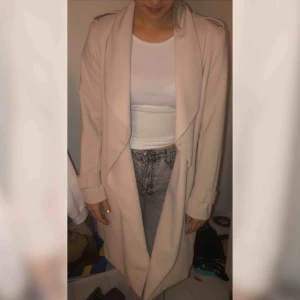  - Beige kappa i storlek 42. brukar ha 38-40 men tycker den satt snyggt iallafall. Bälte runt midjan med en knäppning i guld. Är 167 cm lång och den går till knäna på mig ungefär, kan skicka fler bilder om det skulle vara så! Knappt använd