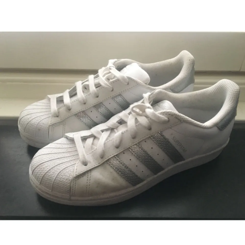 Vita Adidas Superstar med silvriga ränder. Använda en del, men fortfarande i fint skick. . Skor.