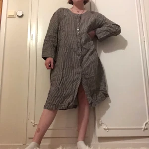 Skjortklänning i XL - Skjortklänning i XXL men passar de flesta. Grå och svart randig. Knappar vid handleder och längs mitten av klänningen. En bröstficka på höger sida. Kan ha den öppen som en jacka eller liknande.
