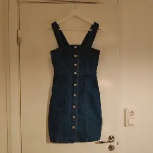 En jeansklänning med knappar på framsidan och fickor. 