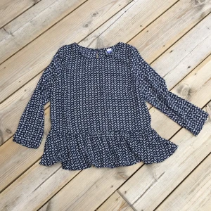  - Söt blus med en knapp i ryggen, rak modell med en volangdetalj nertill.  Mörk marin med vita små mönster detaljer