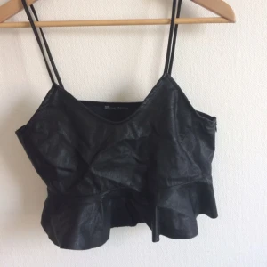  - Svart magkort topp i fejkskinn. Volanger längs ner. Från zara. Aldrig använd! 