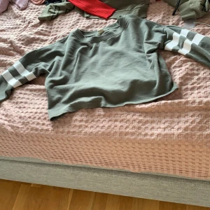 Grön tröja - En grön tröja som är lite kortare vid magen och långärmad med vita linjer på ärmarna