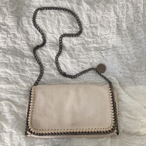 Stella McCartney väska  - En Stella McCartney inspirerad väska. Vit med mörka kedjor. En magnetisk knapp som stänger den och mycket förvaringsmöjligheter inuti, även en deahkjedja som stänger väskan. Möts upp i Stockholm, kan också frakta men isåfall står du själv för frakten. 