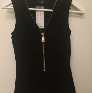  - Snygg svart topp med guldig dragkedja som du kan knäppa hur du vill! Aldrig använd, prislapp kvar