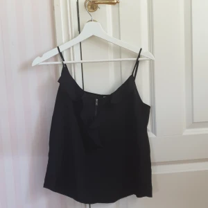 Svart linne med volang ✨ - Svart linne med volang o dragkedja vid bröstet. Använd men i fint skick. Reglerbara band❤