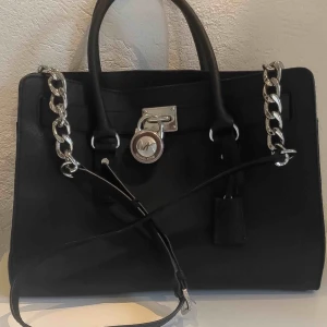  - Saffinoläder, Silver och läderaxelrem (43cm) med två handtag. Väskan har flera fack inuti.  Storleken på väskan är: 37 cm lång x 14 cm bred x 27 hög.  Sparsamt använd! Köpare betalar frakt 🐯