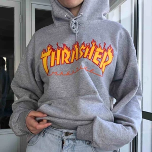  - En grå fläckfri thrasher hoodie, med röd orangeast/gult tryck. Knappt använd, köpare står för frakt