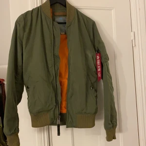 Alpha Bomberjacka - Grön bomberjacka från alpha, strl L passar även M. Jackan har fått på sig 2 små inte så synliga röda fläckar som inte går bort. Nypris 1 600kr