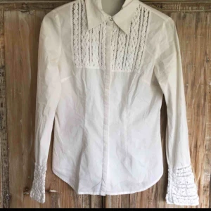  - Vit skjorta med broderi på ärmarna samt på bröstet, med gömda knappar hela vägen ner. Fint skick, knappt använd. Frakt ej inkluderat.