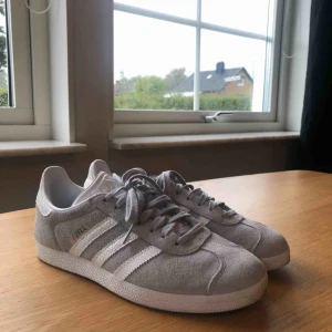  - Säljer ett par ny gazelle skor från Adidas i mycket bra skick!  Skorna är i mocka i en ljusgrå färg, med guld detaljer. Skorna är använda ett fåtal gånger. Storlek: 39 1/3  