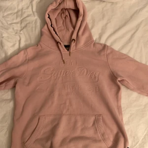 Superdry hoodie - Säljer denna jättefina hoodie ifrån superdry, köpt i London för ett tag sen men aldrig använd. I en fin rosa färg men text på magen! Skriv ifall du skulle vilja ha fler bilder elr har frågor🥰köpt för 499kr, köparen står för frakten 
