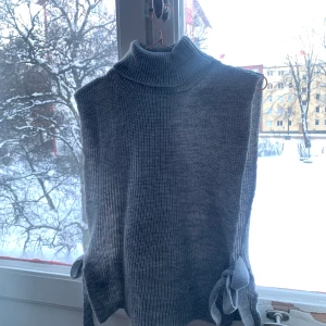Grå stickad väst - Grå stickad väst med knytningar på sidan. Passar XS-M beroende på hur man vill att den ska sitta. 