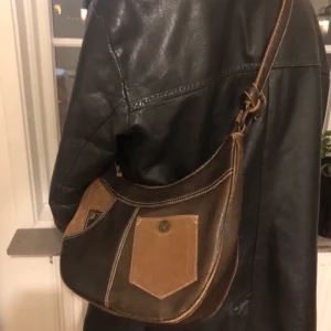 Secondhand väska - En mörkbrun väska med ljusbruna detaljer i fake skinn! Sitter snyggt och är väldigt rymlig❤️ hör av er vid intresse!