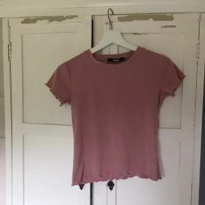  - Rosa T-shirt med volang  Märke: Bikbok Storlek: XS Skick: Fint, väldigt lite använd  Tröjan fraktas. Priset är exklusive kostnaden för frakten. 