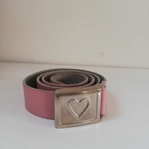 Ljusrosa läderskärp 75cm  - Säljer ett super fint läderskärp i ljusrosa med ett fint metallspänne med et t hjärta på. Ganska bra skick. 75cm skulle motsvara S/M.😚