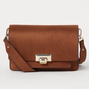 Oanvänd handväska från H&M - Jättefin handväska från H&M som tyvärr aldrig kommer till användning! Helt oanvänd, lappar sitter kvar. Rymlig, med flera fack och justerbart/utbytbart band. Cirkapris så buda gärna!