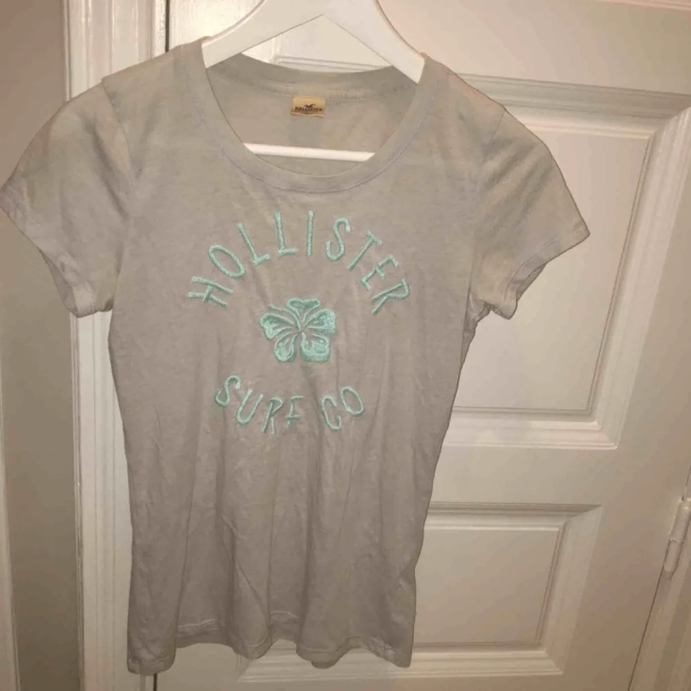 En ljusgrå t-shirt med ljusblå text från Hollister. Vi möts gärna upp i Stockholm men om frakt betalar köparen det . T-shirts.