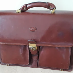  -  Datorväska / portfölj i vackert brunt kalvläder. Märke Pierre. Klassisk utformning som dessutom rymmer laptop upp till 16–17 tum. Lås med nyckel, stort datorfack med dragkedja, två rymliga fack med plats för mobil, laddare, dokument, block, skrivredskap, personliga ägodelar mm. Två mindre yttre fack på framsidan, rymmer mindre läsplatta, bok el. dyl. Fack med dragkedja bak. Handtag och axelrem. Bredd: 42 cm, höjd: 30 cm, djup: 15 cm. Nyskick. Nypris ca 2.500 kr. Säljes 500 kr.