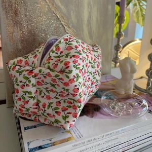 Blommig necessär - Necessär med blommor som yttertyg,ett vitt mellantyg(syns inte)och lila rutigt innertyg. Ca 20cm lång,12cm bred och 10 cm hög. Jag hobbysyr bara så kan inte lova raka sömmar eller 100% felfritt. Skickas med frimärke: 22kr och filmar när den skickas. Är din för 100kr plus porto