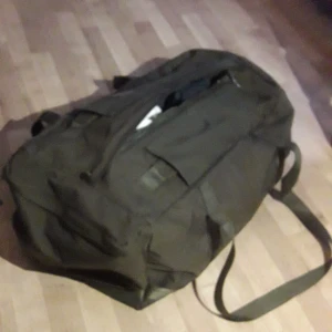 Bärsäck 2000 hemvärnets orginal - Grön väska av bagmodell. Kan med hjälp av bärremmar som fälls in bakom tygflärpar bäras på ryggen. På ena kortsidan finns en ficka som stängs med dragkedja. Längs hela väskans ovansida sitter en dragkedja för att stänga väskan.LÄNGD 605.0 mm HÖJD 260.0 mm BREDD 375.0 mm