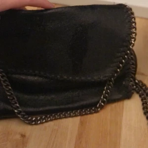 Svart glittrig väska med kedja - Snygg väska med kedja! Väskan stängs med en magnet knapp. Har knapp på insidan! Färg: SVART mixat med glitter  Tvättråd: 30 grader 