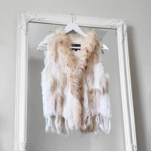 Vit pälsväst Hollies xs - Färg: vit.  Strl: XS.  Äkta päls: kanin och raccoon (tvättbjörn). Pälsväst med fransar nertill från Hollies. Sluts igen med 3 stycken hyskor framtill, passar perfekt under en tunnare jacka på vintern eller över en skinnjacka. Mycket fint skick!