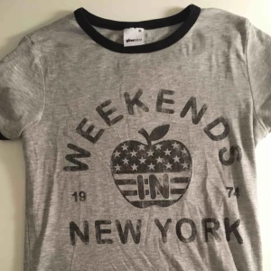  - Grå T-skirt med svart tryck. Sitter ganska tajt på kroppen. 