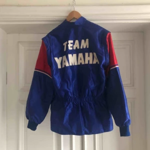  - Racingjacka från TEAM YAMAHA. 90-tal. Armarna kan tas av så blir det en väst. Trevligt skick men dragkedjan behöver sys fast i nederkant, enkelt fixat. Kan hämtas i Uppsala eller skickas mot fraktkostnad.