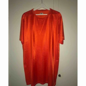  - Orange (ser lite mörk ut på bilderna) stor tisha/t-shirtklänning i glansigt material. Använd 1 gång! Frakt tillkommer.