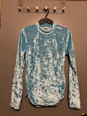 Blå sammetstopp med snörning H&M - Supersnygg blå långärmad från Cubus. Toppen har en unik snörningsdetalj på sidan som ger en cool twist. Perfekt för dig som vill sticka ut lite extra med en glansig och trendig look.