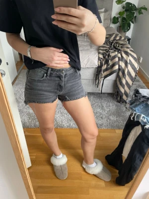Grå denimshorts med rå kant - Snygga grå jeansshorts med rå, fransig kant och klassisk femficksmodell. Shortsen har en hög midja och är tillverkade i bomull. Perfekta för en avslappnad och trendig look.
