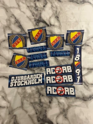 Djurgården klistermärken samling - Samling med olika Djurgården-klistermärken i blå, gul, vit och röd färg. Innehåller DIF-emblem, texter som 'ULTRAS', 'FRIHET', 'DJURGÅRDEN STOCKHOLM', 'ACAB' och siffrorna 1891. Perfekt för att visa ditt stöd för laget. 14 st