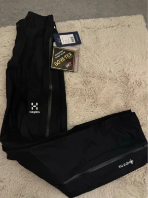 Svarta skalbyxor Haglöfs Gore-Tex XS - Säljer ett par svarta skalbyxor från Haglöfs i modellen L.I.M Pant Women. Byxorna är tillverkade i lätt och smidigt Gore-Tex Paclite Plus-material som är vattentätt och andas. Långa dragkedjor längs benen och diskret logga på låret. Perfekta för uteliv och äventyr. Byxorna är helt oanvända.