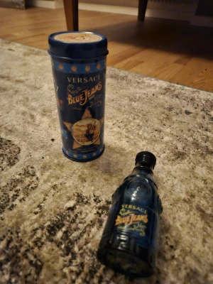 Versace Blue Jeans Man parfym - Versace Blue Jeans Man parfym i en blå glasflaska med detaljerade reliefmönster och Versaces ikoniska Medusa-huvud. Flaskan har en unik, retroinspirerad design med gul och röd text på framsidan. Perfekt för dig som gillar klassiska och fräscha dofter. Kommer med boxen och är äkta.😀