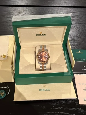 Rolex Datejust tvåfärgad klocka - Säljer en lyxig Rolex Datejust klocka med tvåfärgad länk i silver och guld. Urtavlan är kopparfärgad med datumvisning och klassisk Rolex-logga. Klockan levereras i originalbox med certifikat och tillbehör. Perfekt för dig som vill ha något exklusivt.