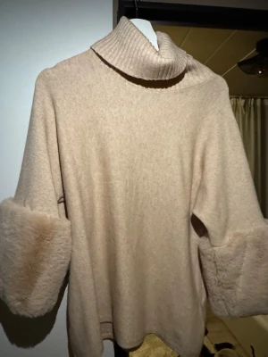 Beige polotröja från Gemini - Säljer en beige stickad polotröja från Gemini med bred ribbad krage och fluffiga ärmslut. Tröjan har en avslappnad passform och är gjord i mjukt material som känns lyxigt. Perfekt för dig som gillar trendiga detaljer och vill ha något extra till hösten eller vintern.