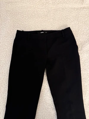 Svarta lågmidjade kostymbyxor från BikBok - Snygga svarta kostymbyxor från BikBok med klassisk rak passform och hällor för skärp. Byxorna har diskreta sidofickor och är perfekta för en clean och stilren look. Materialet känns mjukt och följsamt.