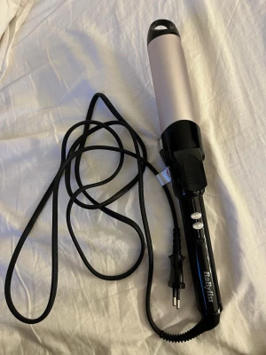 BaByliss locktång svart/silver - Locktång från BaByliss i svart och silver med sladd och två vita knappar på handtaget. Cylindrisk form och ergonomiskt grepp, perfekt för att skapa stora lockar eller vågor. Tillverkad i plast och metall med klassisk design. Locktången har använts 2 ggr men har tvättats av sen dess💕