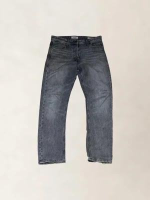 Jack & jones jeans - Säljer ett par grå jeans från jack and jones med rak passform och klassisk femficksdesign. Perfekta för en avslappnad och trendig stil. Modell: loose chris. Storlek 28/30.