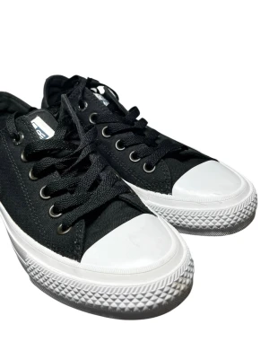 Converse Chuck Taylor All Star II OX – Svart  - Klassiska svarta Converse sneakers med vit tå och sula. Skorna har lågt skaft, svarta skosnören och metallfärgade öljetter. Ovandelen är i canvas och sulan i gummi. Perfekta för en avslappnad och stilren look.