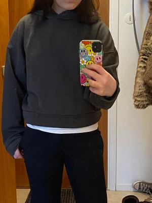 Mörkgrå cropped hoodie - Säljer en enkel och stilren mörkgrå cropped hoodie med huva. Hoodien har en avslappnad passform och bred mudd nertill. Perfekt för en chill och avslappnad look. Materialet känns mjukt och bekvämt mot huden. Kan vara lite nopprig. Står L på lappen men passar S. Den är typ grå/mörkgrön