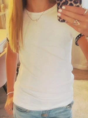 Vit t-shirt med pärldetaljer Zara - Snygg vit t-shirt från Zara med korta ärmar. Ärmsluten har svarta band dekorerade med pärlor som ger en unik touch. Tillverkad i mjuk bomull, perfekt till jeans eller kjol. Enkel men ändå trendig design.