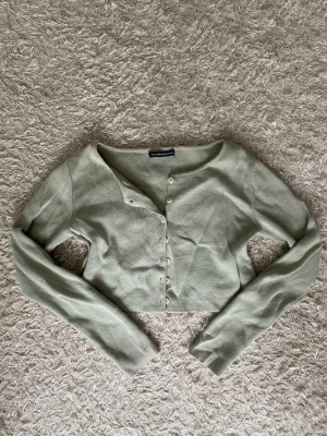 Ljusgrön cropped kofta Brandy Melville - Snygg ljusgrön cropped kofta från Brandy Melville med långa ärmar och rund hals. Koftan har ribbad struktur och knäpps framtill med små vita knappar.