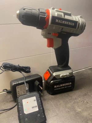 Malmbergs sladdlös borrmaskin 18V - Säljer en sladdlös borrmaskin från Malmbergs med 18V lithium-ion batteri och laddare. Maskinen är svart och grå med röda detaljer och har ergonomiskt handtag. Perfekt för hemmafix och DIY-projekt. Laddare och batteri medföljer.