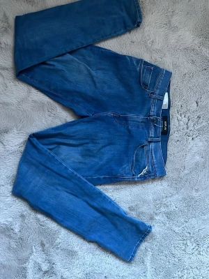 Blå slim fit jeans från Replay - Snygga blå slim fit jeans från replay med klassisk femficksdesign och coola detaljer på bakfickorna. Jeansen har normal midja och är gjorda i mjukt denimtyg med lite stretch för extra komfort. Perfekta till en avslappnad stil.