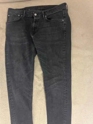 Svarta slim fit jeans från Nudie - Snygga svarta slim fit jeans från Nudie Jeans med klassisk femficksdesign och diskret vågmönster på bakfickorna. Jeansen har en något tvättad look och är tillverkade i mjuk bomullsdenim 