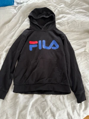 Svart hoodie från FILA med logga - Svart hoodie från FILA med stor färgglad logga i rött och blått.❤️🩵 Klassisk ficka framtill, ribbade muddar och huva. Perfekt för en chill och sportig stil. Materialet är mjukt och bekvämt, troligen bomullsblandning💙✨❄️