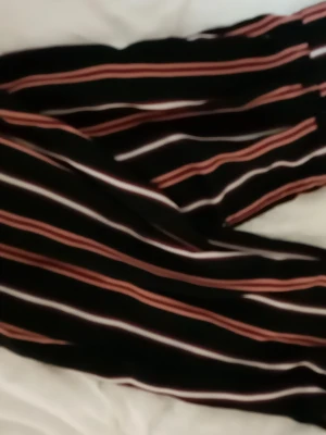 Randiga byxor med rosa och vita ränder - Snygga byxor med svart bas och långa rosa och vita ränder. Perfekta för dig som gillar en trendig och avslappnad stil. Byxorna har en mjuk känsla och elastisk midja för extra komfort.