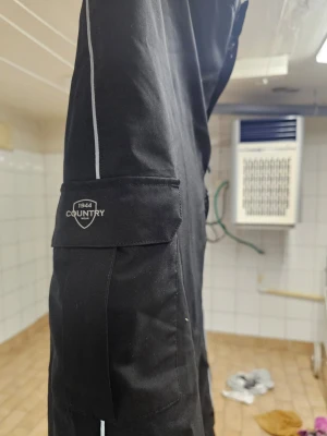 Svarta cargobyxor från Country - Säljer ett par svarta ridbyxor från Country med praktiska fickor på sidorna och diskret logga på ena benet. Byxorna har en rak passform och är tillverkade i ett slitstarkt material. Relax på sidan 